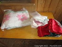 Quilt partially wrapped in plastic showing pink flower designs and additional folded table linens in white and red.