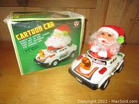 Image of Santa Claus cartoon battery operated car next to original box showing the toy in white plastic with red Santa figure and colorful decals.