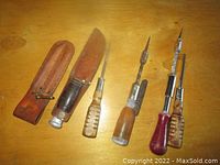 Photo showing vintage fixed blade knife with wooden handle and leather sheath next to three wooden-handled screwdrivers.