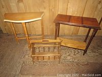 Photo showing two small wooden tables and a wooden magazine rack grouped together on a wooden floor with a wood-paneled background.