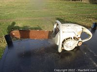 Side view of the vintage white chainsaw showing rusted chain blade, metal body, and handle.