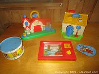 Lot overview showing Fisher-Price barn and house, tin drum, water ring game and noise maker.