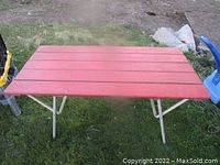 Top view of red wooden slatted folding patio table with metal legs on green grass.