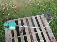 Full side view of the Weed Eater XR80 gas string trimmer laid on a wooden pallet on grass showing the entire tool including engine housing, shaft, handle, and black plastic trimmer guard.