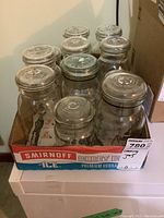 Eleven clear glass canning jars arranged inside a branded Smirnoff Ice box, visible tops with glass lids and some metal rings.