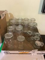 Overview of 12 glass canning jars in a cardboard box, mixed sizes, clear glass, some with screw lids, some clamp lids.