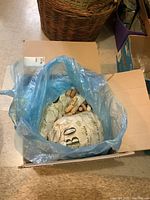 Cardboard box containing bags filled with used wine corks, some visible through a blue plastic bag.