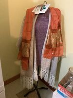 Dress form displayed with a white patterned shawl and an orange silk scarf draped over it