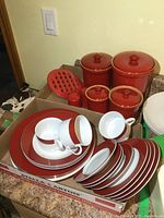 Photo showing all red canisters with lids grouped together alongside a red utensil holder, salt, and pepper shakers on kitchen counter.