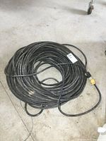 Top view of coiled black heavy duty extension cord showing the yellow female connector plug and some dirt marks on the cord.
