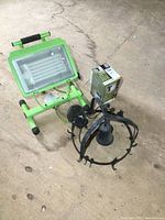 Photo showing green portable fluorescent work light on stand, metal hanging light fixture, and boxed fluorescent wall lantern bulb.