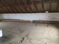 Long wide shot of storage area with stacks of wood lumber against the wall under sloped ceiling.