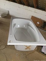 Top/angled view of white fiberglass bathtub showing interior and armrests with minor surface dirt and peeled plastic film
