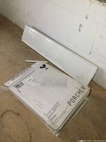 White metal radiant hot water heater panel leaning against a wall next to a Porcher branded box on the floor,