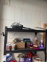 Photo of a shelf with assorted Christmas decorations, boxes, and figurines including ornaments and nutcracker.