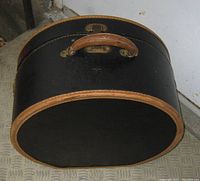 Photo showing the front leather handle, black exterior with tan leather trim and metal latch.