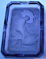 Top view showing detailed intaglio relief of a nude woman seated by a swan in natural surroundings within a rectangular faceted purple glass ashtray.