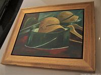Framed oil painting on board showing two beige cloche hats on a dark green container and a parrot in the background.