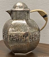 Front angled view showing detailed figural repoussé panels, spout, lid and woven handle wrapping on creamer jug tea pot.