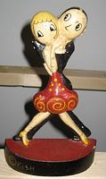 Front view of enameled cast iron doorstop depicting a stylized dancing couple with the signature '© Fish' visible on the base.