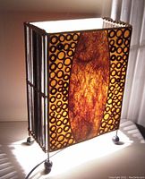 Lamp lit showing glowing central woven fibrous panel and circular dark rings on side panels, supported on round footed base.