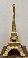Front view of golden Eiffel Tower statue showing 'PARIS' etched on the front, revealing the display area inside the base.
