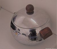 Front angle view of the polished metal ice bucket displaying the wooden handles and lid knob, with visible penguin figures on the body.