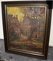 Front angled view of the framed oil painting showing the village scene with a large tree and buildings in warm tones.