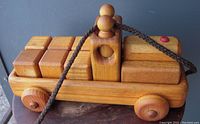 Close-up of the handcrafted wooden truck pull toy showing the natural wood blocks on the bed, round wheels, the round-headed driver figure with hole for pull rope, red button detail, and braided pull rope.