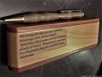 Close-up side view of the black walnut wood pen placed on top of the fitted wood case with the engraved plaque visible.