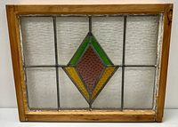 Front view of stained glass window panel showing diamond pattern with green, yellow, and purple panes in wooden frame.