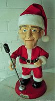 Full front view of Bing Crosby Christmas figure in Santa outfit with microphone and control device on round base with name plaque.