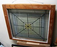 Front view of vintage wood framed stained glass window with wire hanging and geometric rectangular design.