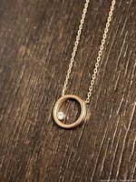 Close-up of the circular gold pendant with a single small diamond inside on a wood surface.