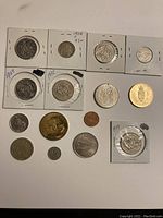 Coins arranged on a surface, some in cardboard holders with year and price labels.