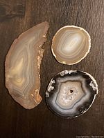 All three agate slices shown on dark wood surface for size and detail comparison