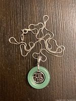 Close up of the sterling silver chain and jade pendant with silver Chinese character centerpiece on a wood surface.