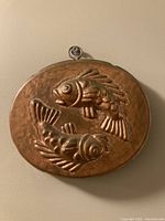 Front view of oval copper fish jello mold with detailed embossed twin fish design and hanging loop.