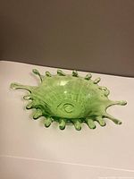 Green glass art dish viewed from a side angle showing the irregular spiked rim and textured surface.