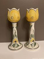 Front view of two hand painted yellow daffodil Delft candlesticks showing tulip-shaped tops and painted floral designs on stems and bases.