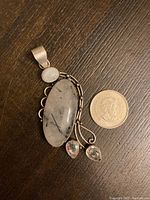 Front view of a large sterling silver pendant with 3 gemstones and a quarter for scale on dark wood background.
