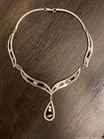 Front view of Mexican silver necklace with shell inlay and teardrop pendant displayed on a dark surface.