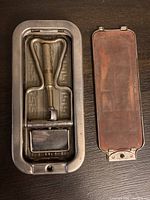 Metal box containing vintage Rolls razor with integrated strop, lid removed and placed aside