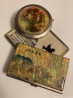 Close-up of the three items showing detailed artwork on the cigarette cases and compact mirror.