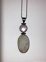 Pendant necklace with oval crystal and round pearl in sterling silver setting, shown on white background.