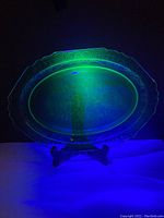 Uranium glass plate under black light displaying bright green glow and intricate Art Deco pattern.