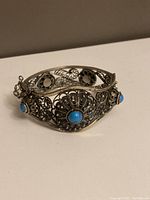 Close-up angled view showing the intricate filigree metalwork and blue stones on the bracelet.