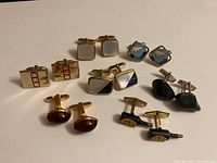 Seven pairs of vintage cufflinks on a pale surface showing variety of colors and styles