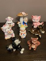 Photo showing eight vintage Japanese porcelain figurines of animals and characters in various poses and colors, arranged on a flat surface against a plain background.