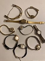 Lot of eight women's wristwatches with various band types and dial shapes shown on a neutral background.